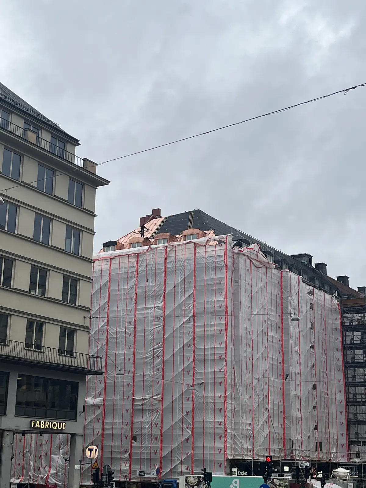 Flerbostadshus inklätt i byggnadsställning med vit väderskyddsduk