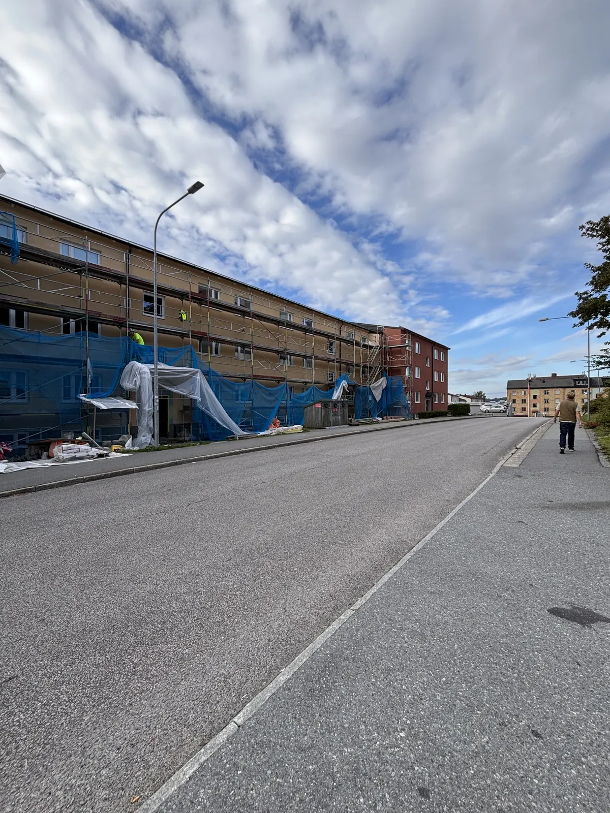Gatuvy med byggnad under fasadarbete täckt av blå skyddsväv