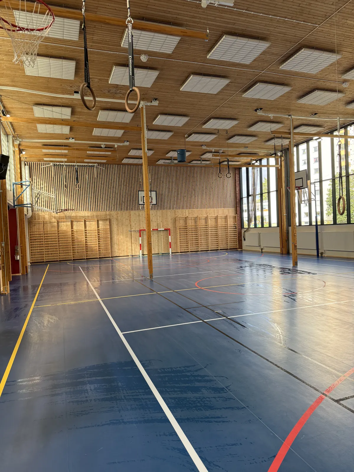 Idrottshall med trätak, basketkorgar och blått sportgolv