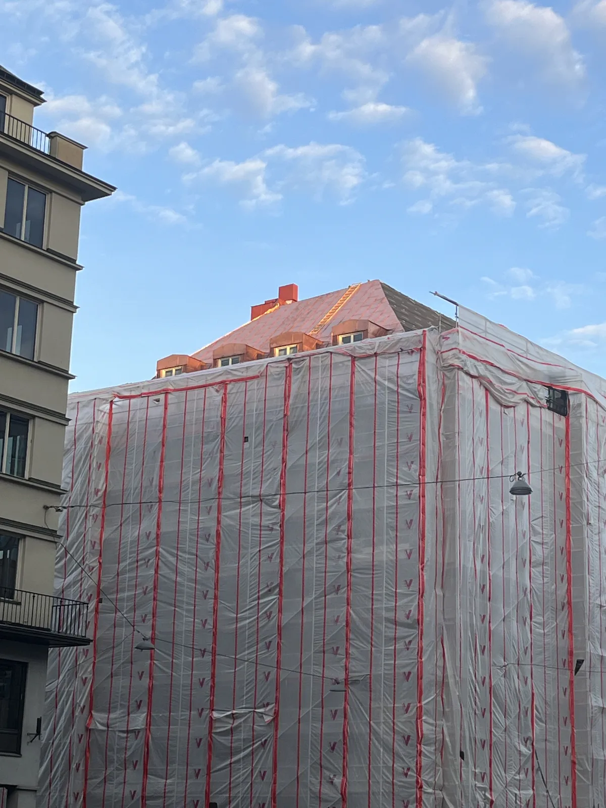 Byggnad täckt av ställning och väderskyddsduk mot blå himmel