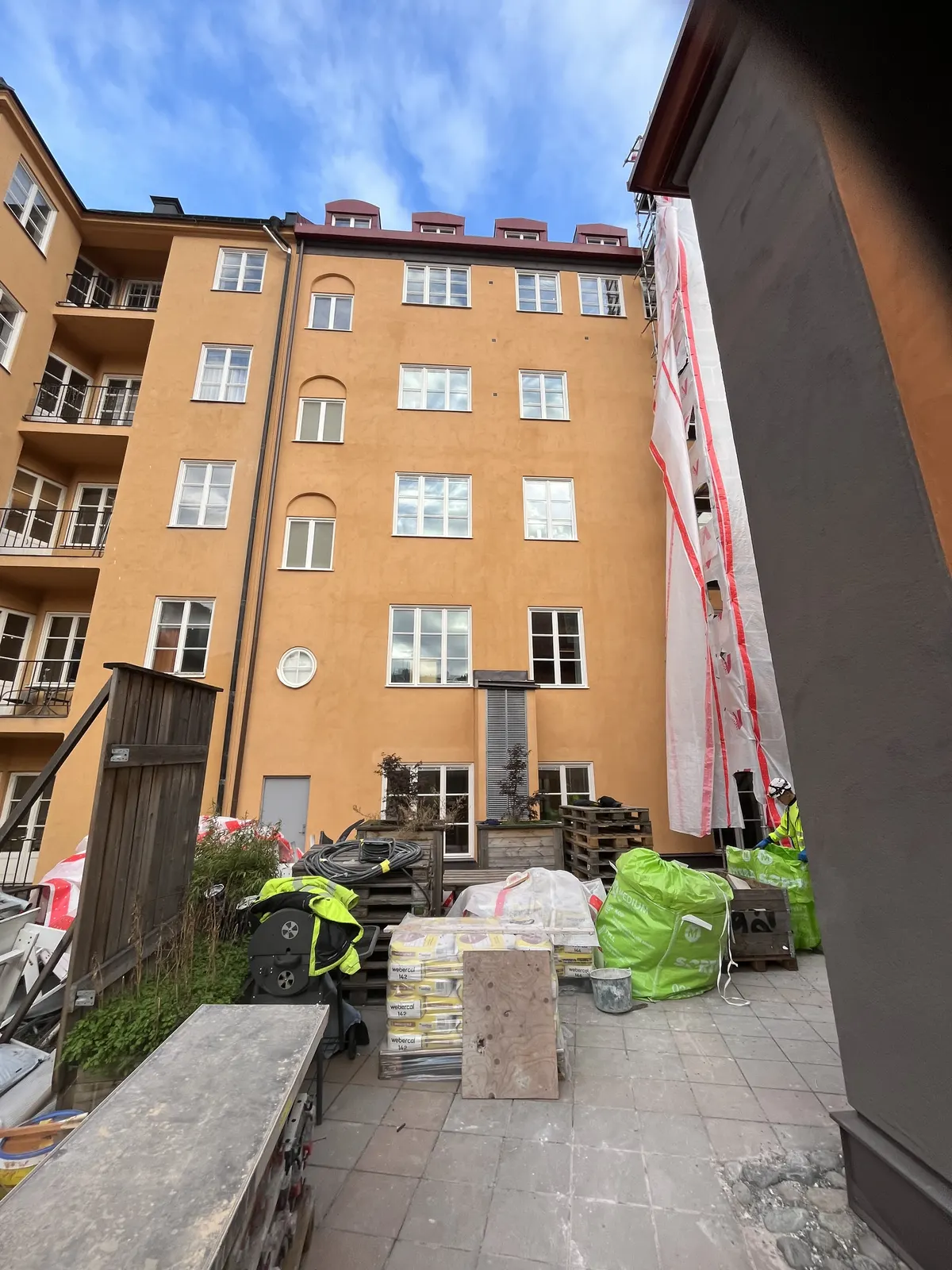 Innergård med byggmaterial och arbetare framför gul putsfasad
