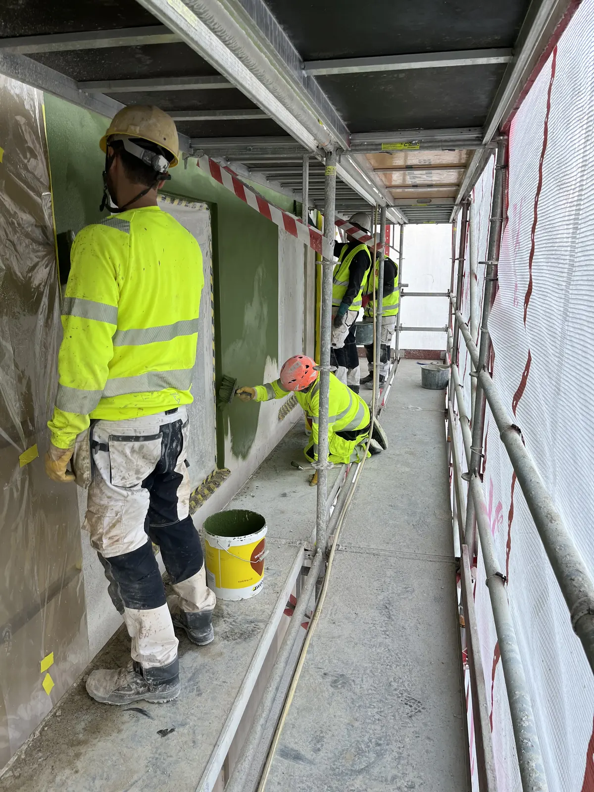Två hantverkare arbetar i ett inbyggt ställningsschakt längs fasaden