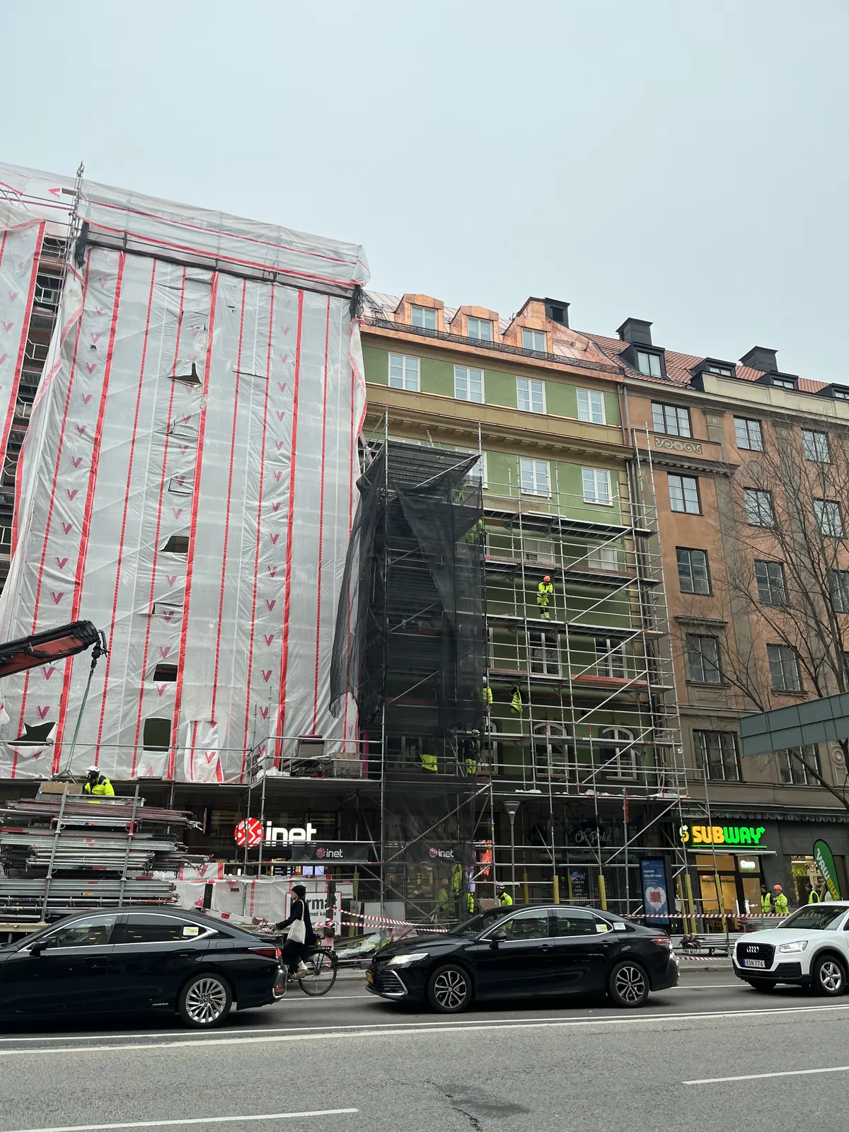 Gatuvy med byggnaden delvis inklädd i ställning och trafik i förgrunden
